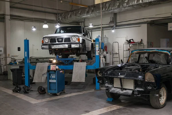 Coche usado blanco Nissan Patrol levantado en un ascensor azul para reparar — Foto de Stock