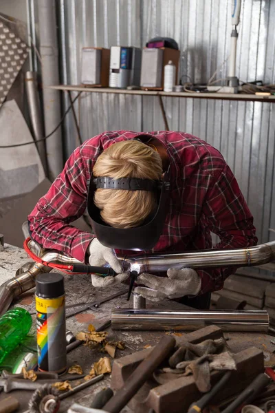 Young guy welder in a checkered red shirt welds a stainless stee