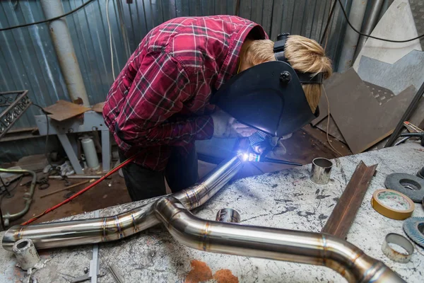 Young guy welder in a checkered red shirt welds a stainless stee