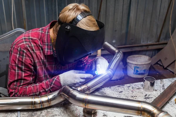 Young guy welder in a checkered red shirt welds a stainless stee