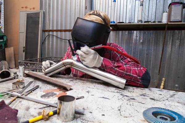 Young guy welder in a checkered red shirt welds a stainless stee