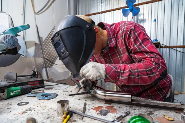 Young guy welder in a checkered red shirt welds a stainless stee