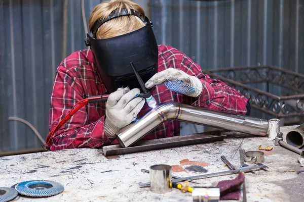 Young guy welder in a checkered red shirt welds a stainless stee