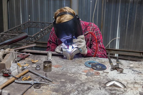 Young guy welder in a checkered red shirt welds a stainless stee