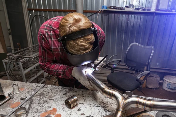 Young guy welder in a checkered red shirt welds a stainless stee