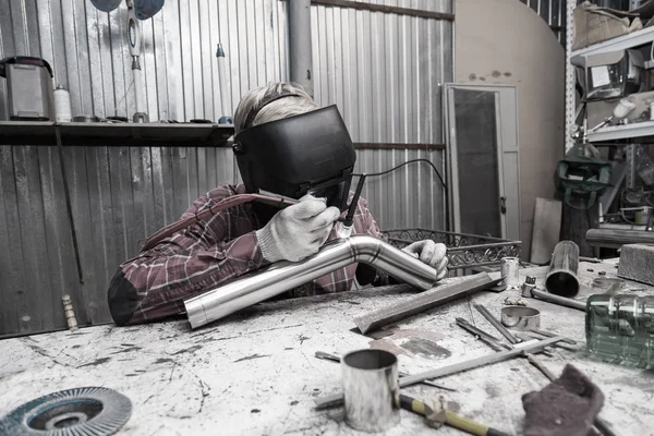 Young guy welder in a checkered red shirt welds a stainless stee