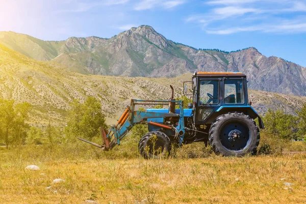 An old blue tractor excavator stands in a field with green and y