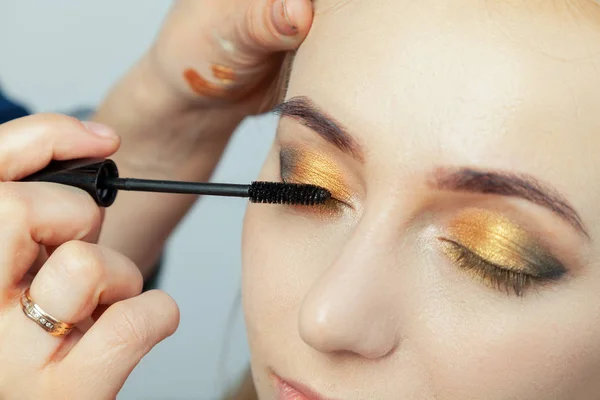 Makeup artist puts on an oriental-style make-up with gold and gr