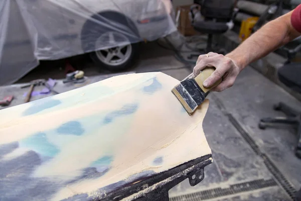 A man prepares a car body element for painting after an accident