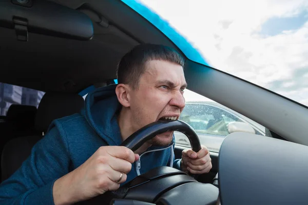 An unbalanced, goosey man bites a car steering wheel from anger — Stock Photo, Image