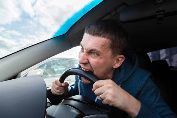 An unbalanced, goosey man bites a car steering wheel from anger — Stock Photo, Image