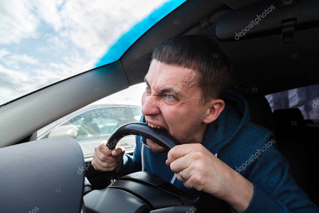 An unbalanced, goosey man bites a car steering wheel from anger 