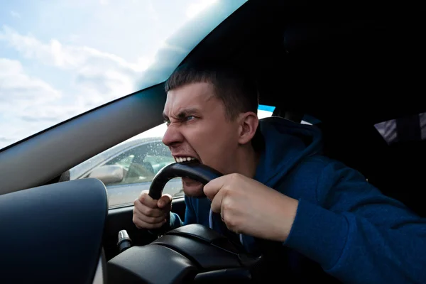 一个情绪化的家伙在开车时咬着汽车的方向盘 — 图库照片