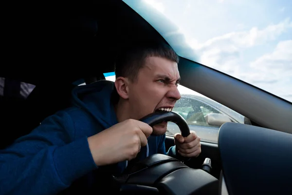 Um cara emocional morde o volante de um carro enquanto dirige — Fotografia de Stock
