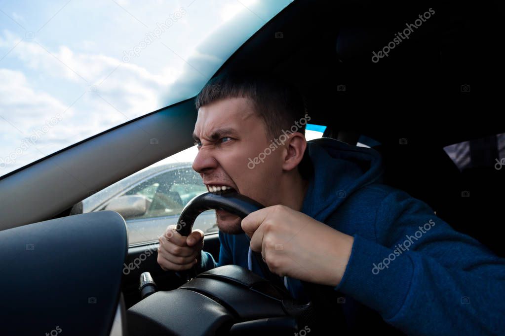 An emotional guy bites the steering wheel of a car while driving