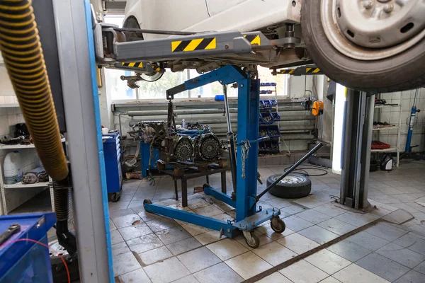 Um carro usado branco levantado em um elevador para o reparo e sob ele um deta — Fotografia de Stock