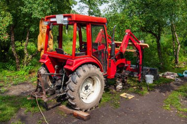 Eski bir kırmızı tarım traktörü repa sırasında ormanda duruyor