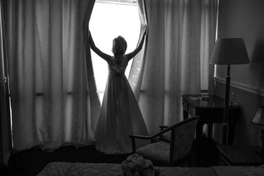 Yatak odası elbiseli sarışın gelin fahişenin perdelerini açıyor.