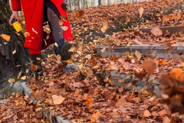 Siyah çizmeli ve kırmızı paltolu bir kız sarı ve kırmızı yapraklı tekmeler.
