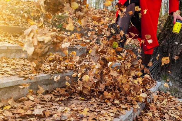 Девушка в чёрных сапогах и красном пальто пинает жёлтую и красную листву. — стоковое фото