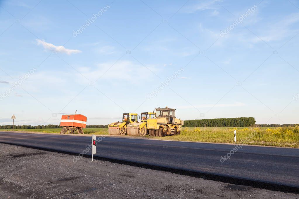 Three large yellow asphalt compactor standing on the side of the