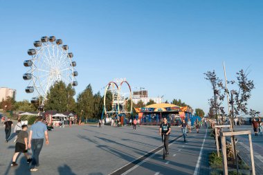 Scooterlar ve patenciler parkta iki büyük dönme dolaba karşı.
