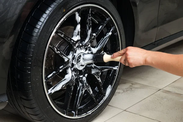 A male worker washes a black car with a special brush for cast w — Stock Photo, Image