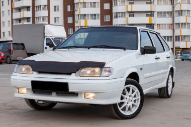 Novosibirsk, Rusya - 05 / 20 / 2020: Otomotiv endüstrisinin Lada markasına ait yeni bir Rus arabası modern beyaz serinin VAZ modeli 2114 kentsel arka planda satışa hazır yanan farlarla birlikte.