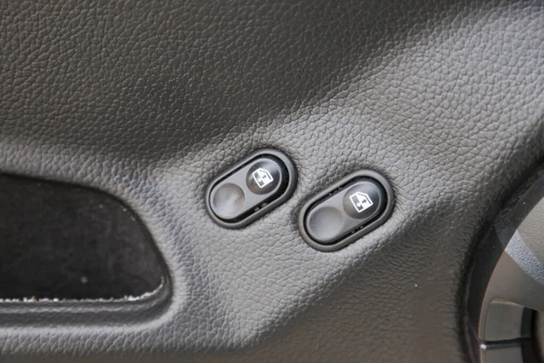 Two black window adjustment buttons with white marks on the plastic panel of the door next to the handle of an old Russian car close-up in front of a dry-cleaner.