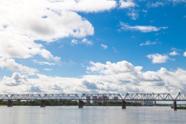 Novosibirsk 'teki Ob nehri üzerindeki demiryolu köprüsü beyaz bulutlu mavi bir gökyüzünün altında. Rusya 'nın resimli manzaraları.