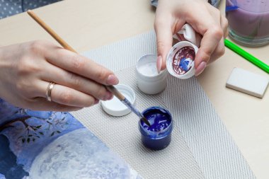 Bir kadının elinde fırça ve suluboya boya için kapak tutan bir resim ve silgi ile basit bir kalemin yanında karıştırılmış renkler. Bir sanat hobisi..