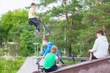Novosibirsk, Rusya - 06.06.2020: Kaykay rampasında bisiklet ve scooter süren bir grup çocuk, bir adam arkadaşlarının önünde havada yüksek hızda zıplayarak bir numara yapıyor.
