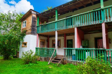 Yazın yaşamak için iki katlı kır evi mavi balkonu ve verandası olan ahşap kulübede, yeşil çimenlerin, çalıların ve mavi gökyüzünün arka planında eski bir merdivende..