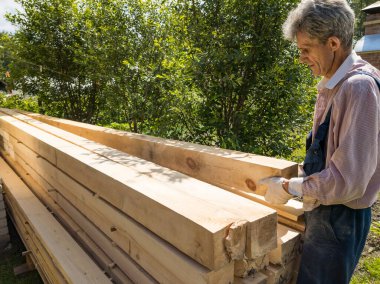 Ülkedeki marangoz bir marangoz, şantiye inşaatı için elinde bir kereste tutuyor. Yeşil ağaçların arka planında mevsimlik ahşap malzemeler kullanılıyor..