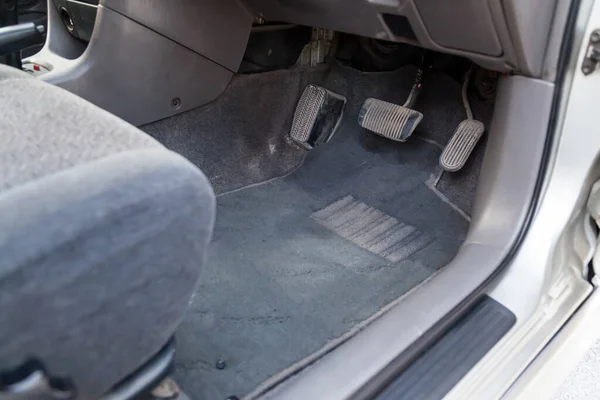 Gray cloth car mat in the interior of a Japanese sedan with three pedals gas, brake and clutch in a car service after dry cleaning.