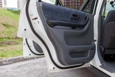 Bir yaz öğleden sonra otoparkta, gri paneller ve tekstil aksanlı beyaz bir Japon cipinin açık yan kapıları..