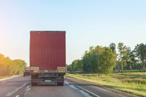 Rear view of a truck with a red body on a road, delivering and transporting cargo by a transport company over long distances through the countryside.