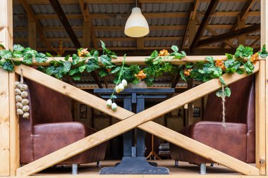 Kahverengi deri koltukları ve ahşap korkulukları olan bir yazlık kafe dekorasyon için suni çiçekler. Çatı katı tarzı açık kafe. Karantinadan sonra restoranların açılışı.