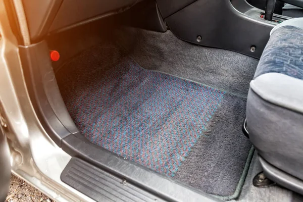 The car mat under the front passenger seat is made of gray textile material in service after a dry cleaning of the passenger compartment close-up during pre-sale preparation.