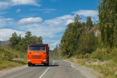 Altai, Rusya - 09.13.2020: Bir yaz günü, yeşil ağaçlar ve mavi gökyüzüne karşı yol üzerinde turuncu bir taksiyle Rus yapımı bir Kamaz kamyonu. İnşaat kargosunun şehir içi teslimatı.