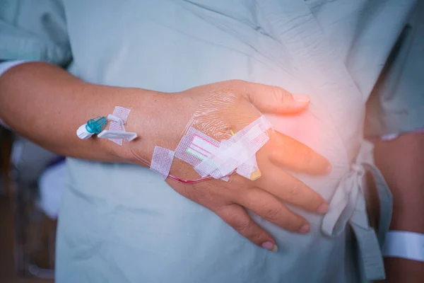 Close up Patients man stomach ache in hospital standing by the bed of a ill sick person, patient rests and saline solution tube intravenous iv drip inserted and stand waiting for the doctor to check.