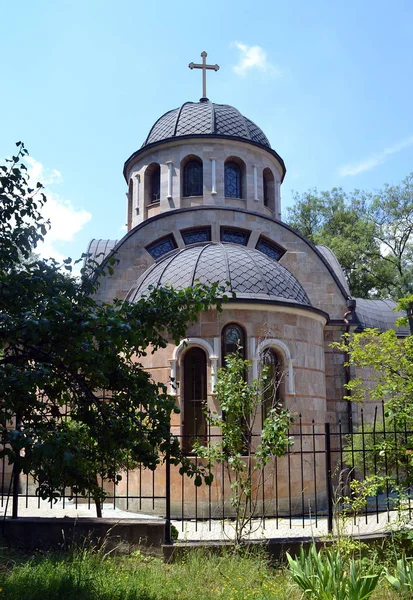 A small church in Sophia, Bulgaria. The building has a rounded shape, the walls are lined with marble. The roof and the dome are covered with black diamond-shaped tiles. Arched windows are taken away by a decorative lattice