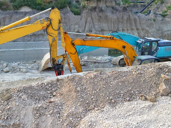Two yellow and one blue excavators in the ditch at the site of the road construction works, side view, summer, day