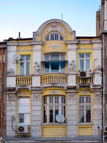 Yellow facade of the house built in the first quarter of the last century decorated with white statues of children, semi-columns and stucco molding