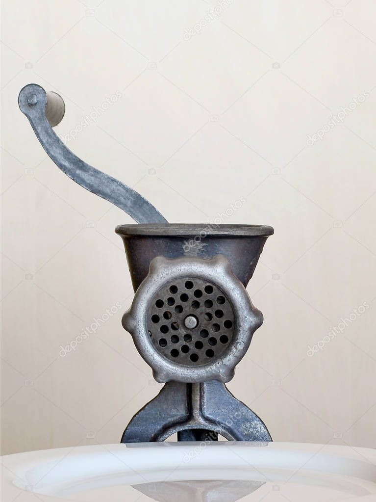 Vintage manual meat grinder and white plate for minced meat on beige background, front view, closeup, vertical frame