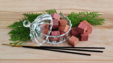 Fragrant wardrobe freshener cubes made of natural pencil cedar wood in a crystal bowl with a lid, few green cypress sprigs and few incense sticks on a wooden background, view from above clipart