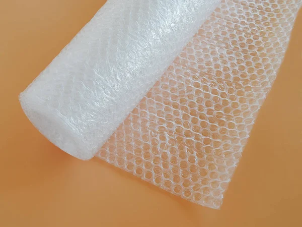 Transparent bubble wrap roll for packaging fragile items on yellow background top view, close up