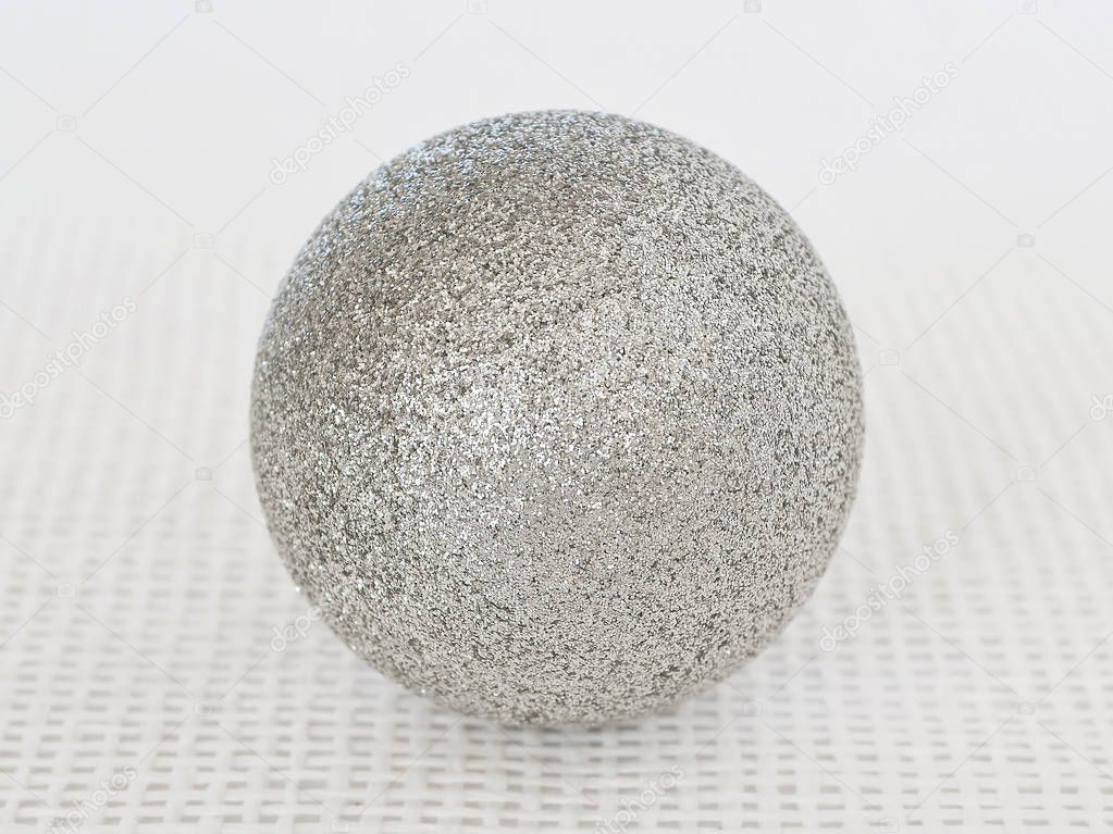 One shiny silver christmas ball with sparkles on a white textural background close up