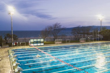 Varna, Bulgaristan, Kasım 2018. Yüzme karmaşık Primorsky Karadeniz kıyısında. Açık spor yüzme havuzu tarafından güçlü sahne ışıkları karanlık sonbahar akşam gökyüzü arka plan üzerinde yaktı.