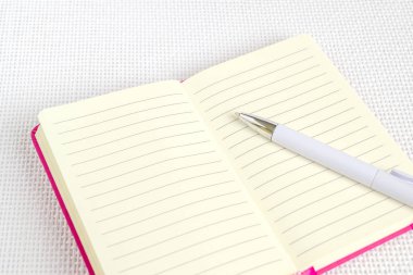Üstünde pembe kapak beyaz arka plan kopya alanı üzerinde açılan defter beyaz tükenmez kalem